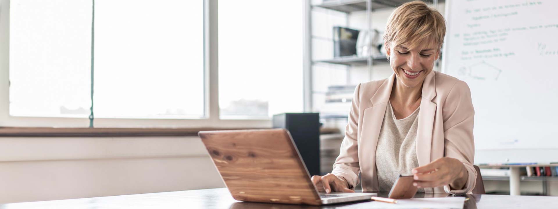 woman sat at desk working on laptop and mobile phone